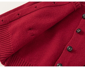 Dettaglio del cardigan in maglia rossa con bottoni neri e decori a fiocco d'oro