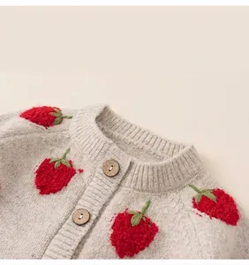 Detail van beige gebreid kindervest met rode aardbeiborduursels en natuurlijke houten knopen