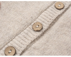 Detailopname van beige gebreid vest met zachte textuur en ronde houten knopen erop
