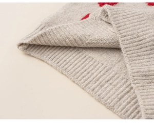 Detailopname van beige gebreid vest met rood hart jacquard en geribbelde manchetten