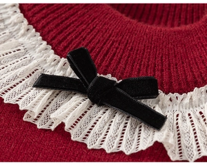 Dettaglio del cardigan in maglia rossa con colletto in pizzo bianco e fiocco in velluto