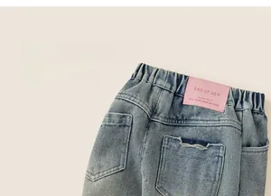 Détail de la taille élastique et de l'écusson en cuir rose sur jean bleu clair