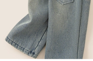 Détail de la texture denim bleu clair et des surpiqûres précises sur le pantalon