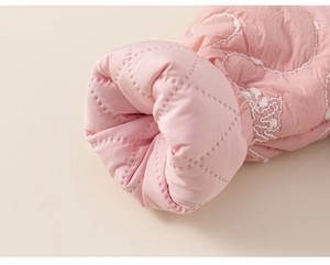 Dettaglio del tessuto trapuntato rosa con ricamo a onde e trama a pois sulla manica del cappotto