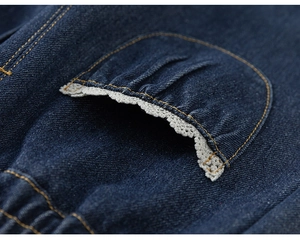Détail d'un jean bleu foncé avec bordure en dentelle crème sur la poche et surpiqûres
