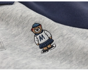 Detail of grey knitted fabric with college-style bear embroidery and navy patchwork