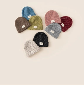 Flat lay of colorful thick knit beanies with white labels for winter in eight vibrant shades