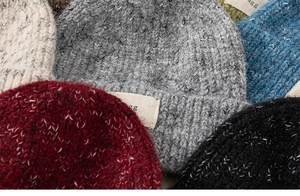Close-up of multicolored chunky knit beanies with decorative fabric labels in five colors