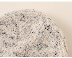 Close-up of chunky knit fabric with textured mixed grey fibers on cream beanie