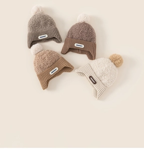 Close-up of knit winter hats with JOURNEY patches and soft pom-poms in four earthy tones