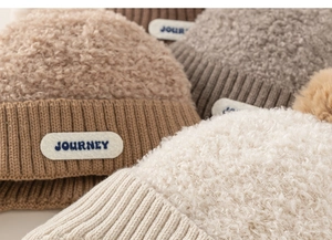 Close-up of winter knitted beanies with sherpa top and Journey label in neutral tones