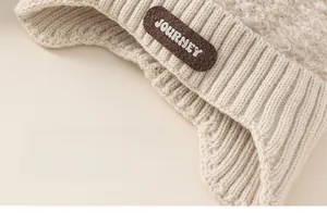 Detail of beige knit earflap hat showing chunky ribbed texture and JOURNEY label
