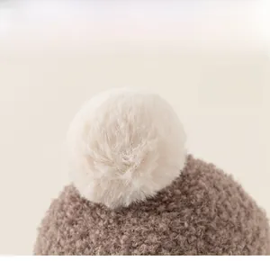 Detail of knit baby beanie showing plush faux fur pompom and textured boucle yarn