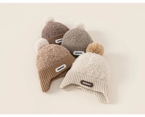 Detailed view of four colors of knit earflap hats with plush balls and Journey patches