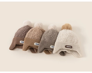 Detail of four knit ear-flap hats with pom-poms and Journey tags in earth tones