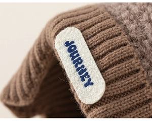 Detail of warm brown knit hat with Journey embroidery and cozy fleece lining texture