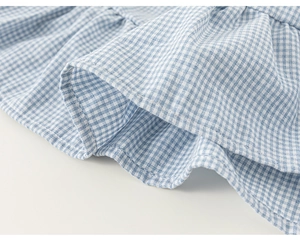 Detail of blue and white plaid fabric with ruffled hem and clean stitching on baby girl dress