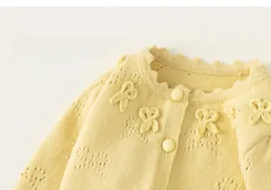 Detail of light yellow knit cardigan featuring hollow butterfly patterns and ruffled collar