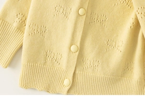 Detail of light yellow knit cardigan featuring hollow butterfly patterns and buttons