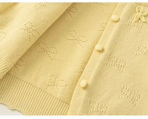 Detail of light yellow knit cardigan featuring hollow bow patterns and fabric buttons