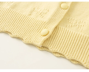 Detail of light yellow knit cardigan featuring ribbed hem and textured round buttons