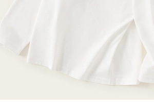 Detailed close-up of side slit hem on a boys minimalist white long sleeve cotton tee