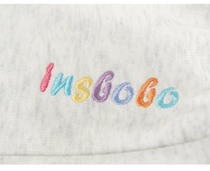 Close-up of colorful insbobo letter embroidery on light gray knit sweatshirt fabric