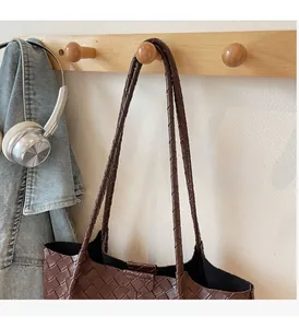 Detail showing the brown woven texture and sturdy dual straps of the leather tote bag