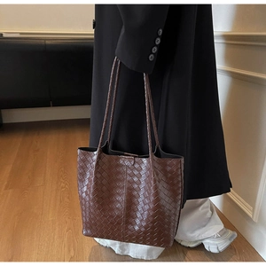 Detail of a dark brown large tote bag with woven texture on a female model shoulder