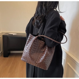 Detail view of woven leather tote bag texture and large shoulder strap in dark brown finish