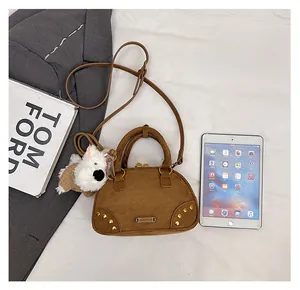 Detail view of brown suede bowling bag with golden rivets and cute plush dog pendant