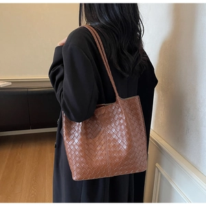 Brown woven leather tote bag shoulder strap detail on black coat during daily commute