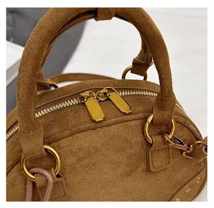 Detail of smooth golden metal zippers and rivet rings on brown suede handbag