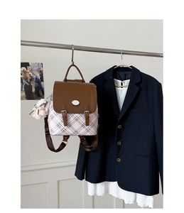Detail view of British style plaid backpack with brown leather flap and fluffy ball pendant