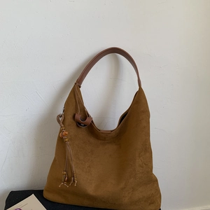 Dettaglio macro della texture in pelle scamosciata marrone con nappa boho sulla borsa