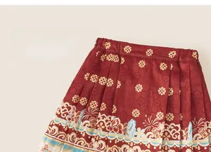 Detailed macro view of red pleated Mamian skirt with golden floral jacquard patterns