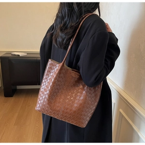 Detail of brown woven faux leather tote bag showing intricate braided texture and slim straps