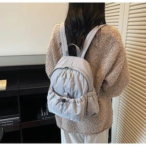 Rear view of model wearing a light grey nylon backpack with drawstring pocket