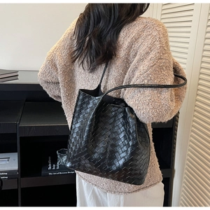 Detail of black woven leather tote bag showing large square grid texture and shoulder strap