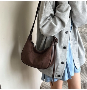 Detail of a dark brown suede half-moon bag featuring elegant side knots and smooth piping