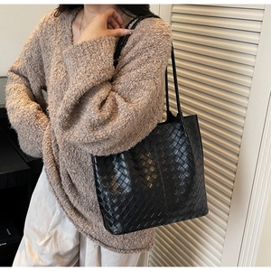 Detail of a black woven leather tote bag shown on model with cozy knit sweater