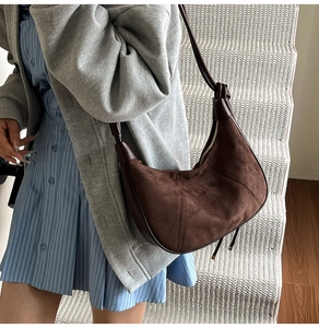 Detail view of dark brown suede crescent bag with stitching on a model's shoulder