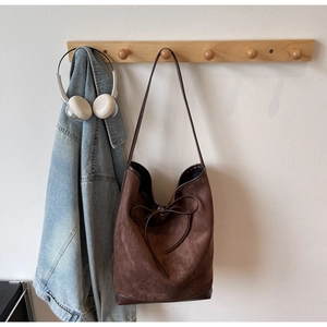 Détail du sac cabas en daim marron avec bordures en cuir et nœud sur un crochet mural