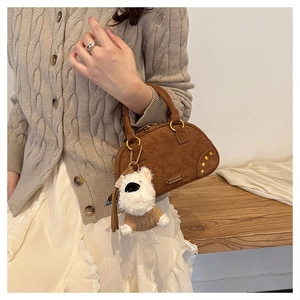 Detailed close-up of brown suede handbag featuring gold rivets and a plush puppy charm