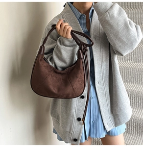 Close-up of retro brown suede crescent bag with stitching detail on a model's shoulder