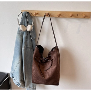 Détail du sac cabas marron en daim mat avec nœud en cuir sur un support en bois