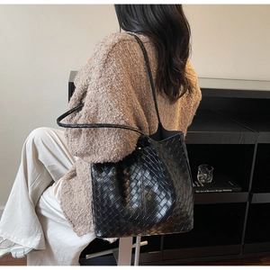 Detail showing high-capacity black woven leather tote bag with a minimalist shoulder strap