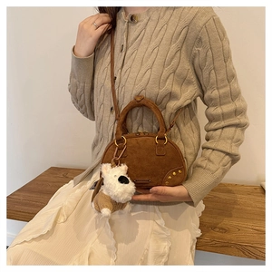 Detail of caramel suede bowling bag featuring gold rivets and plush dog charm