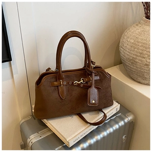 Détail du sac Boston en daim marron avec sangles en cuir posé sur une valise argentée
