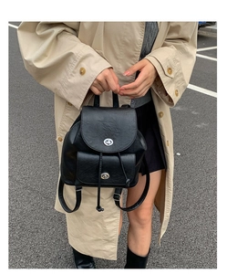 Nahaufnahme des schwarzen Vintage-Lederrucksacks mit Metalldrehverschluss auf beigem Trenchcoat